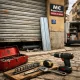 Escena urbana con puerta enrollable medio levantada; herramientas en caja roja. Que compañías ofrecen reparación rápida de puertas enrollables en Madrid.