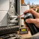 Primer plano de un bisagra y rodillo de puerta de garaje, con mano aplicando lubricante; mejores opciones de mantenimiento preventivo para puertas de garaje en Madrid.